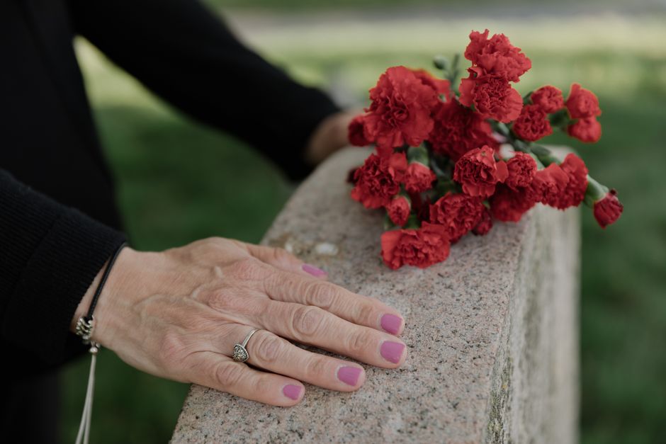 A closer view of a person's hand resting on a stone ledge, showcasing well-manicured nails painted in a muted pink shade. The individual is wearing a black long-sleeve garment, a silver ring with a la